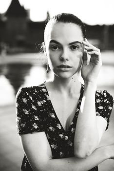 Portrait of a stylish young woman. Brunette with ballerina hairstyle in sundress posing on street, fountain on a background