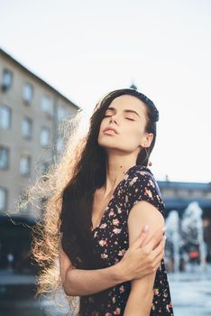 Portrait of a stylish young woman. Brunette with ballerina hairstyle in sundress posing on street, fountain on a background