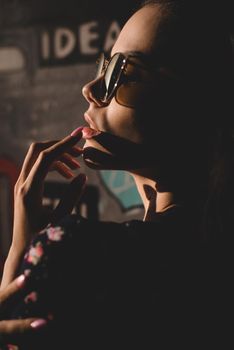 Close-up portrait of stylish young woman. Brunette in sundress posing on street. Finger near her lips