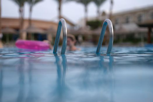 Wet metal handrails on surface of pool. . Summer vacation and lifestyle concept.