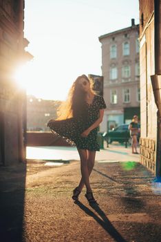 Portrait of stylish young woman. Brunette with curly hair in sundress posing on street.