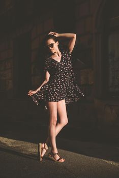 Portrait of stylish young woman. Brunette with curly hair in sundress posing on street.