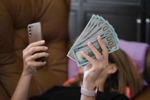 Woman holds smartphone and holds it with dollars. Applications for making money online concept