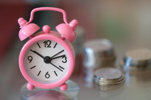 Pink alarm clock compass and stacks of coins. Credit success and growing money back concept