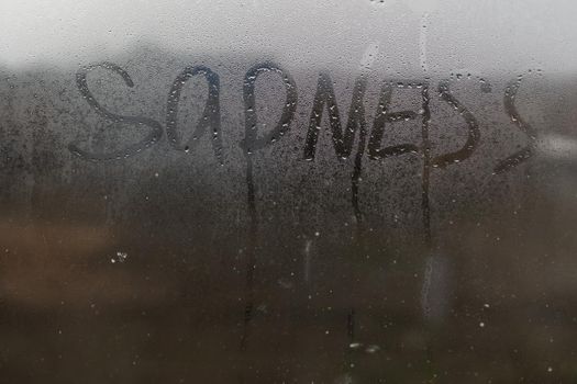 The inscription sadness on the wet window