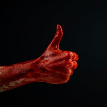 A woman's hand stained with blood shows a thumbs up on a black background