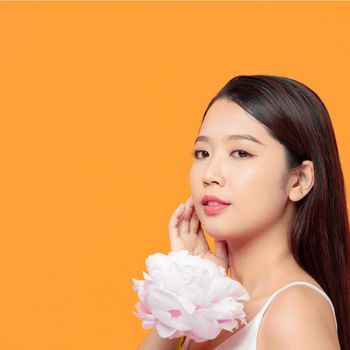 Young woman holding pink peony flower, smiling on yellow background