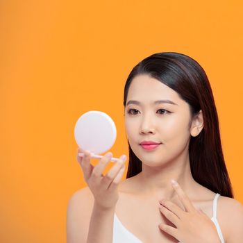 Smiling woman using lipstick on yellow background