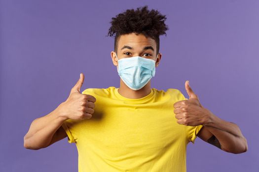 Covid19, healtcare and medicine concept. Enthusiastic happy spanish guy in facial mask, show thumbs-up and smiling with eyes, excited, support social-distancing, prepared for going grocery shopping.