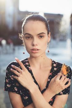 Portrait of a stylish young woman. Brunette with ballerina hairstyle in sundress posing on street, fountain on a background