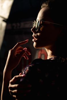 Close-up portrait of stylish young woman. Brunette in sundress posing on street. Finger near her lips