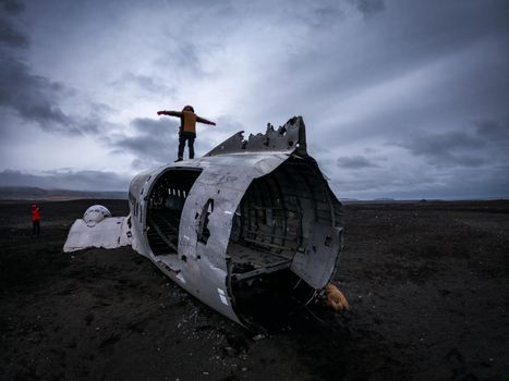 Unrecognizable tourists taking photos on top of the wreck of airplane in Iceland