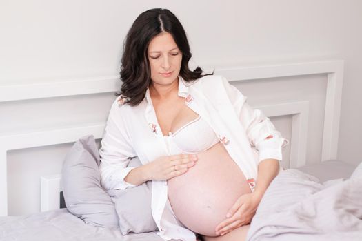 charming pregnant woman in shirt on bed. happy pregnancy.