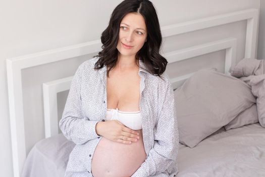 charming pregnant woman in shirt on bed. happy pregnancy.