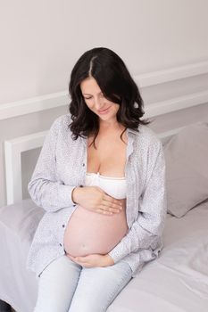 charming pregnant woman in shirt on bed. happy pregnancy.