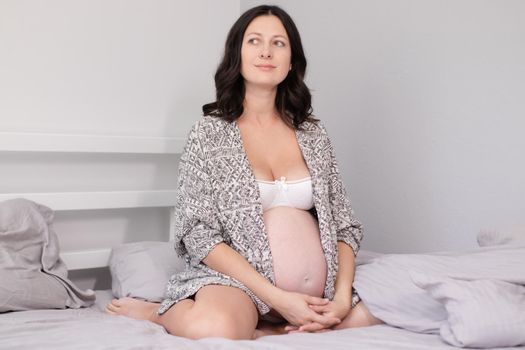 happy pretty woman enjoying pregnancy. mother to be is expecting parent. cute big tummy. pregnant brunette in light room.