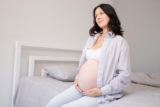 charming pregnant woman in shirt on bed. happy pregnancy.