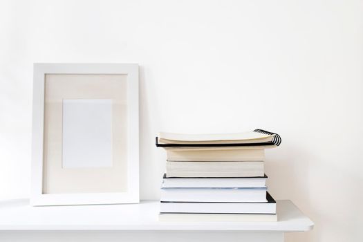 Scandinavian style room interior in white tones. A stack of books, a photo frame on a wooden surface of a shelf. Copy space.