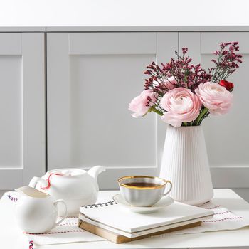 Bouquet of pink Persian buttercups on a white table in front of a chest of drawers. Scandinavian style. Place for text