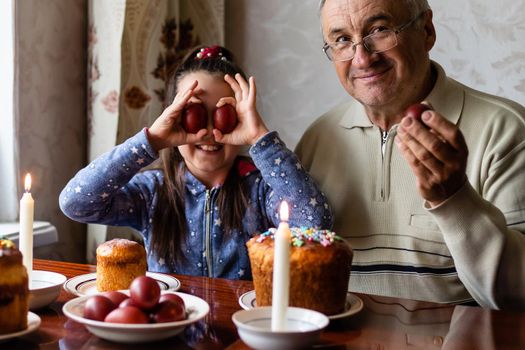 Happy elderly man granfather preparing for Easter with granddaughter. painted colored eggs for Easter.