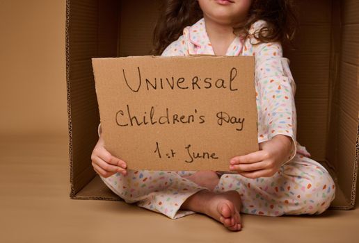 Closeup cardboard banner with social message - World Children's Day on July 1st. Little girl holding a poster calling for respect for children's rights, isolated over beige background with copy space