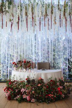 The presidium of the newlyweds in the banquet hall of the restaurant is decorated with candles and green plants, wisteria hangs from the ceiling