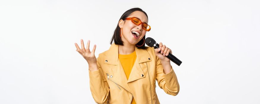 Singing girl holding microphone, performing songs at karaoke, standing over white background. Copy space