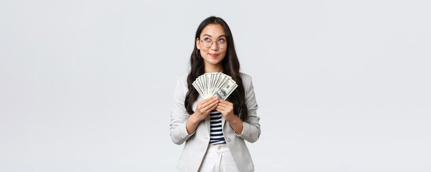 Business, finance and employment, entrepreneur and money concept. Dreamy pleased businesswoman thinking where go vacation and how invest earned dollars, hold cash and looking up thoughtful.