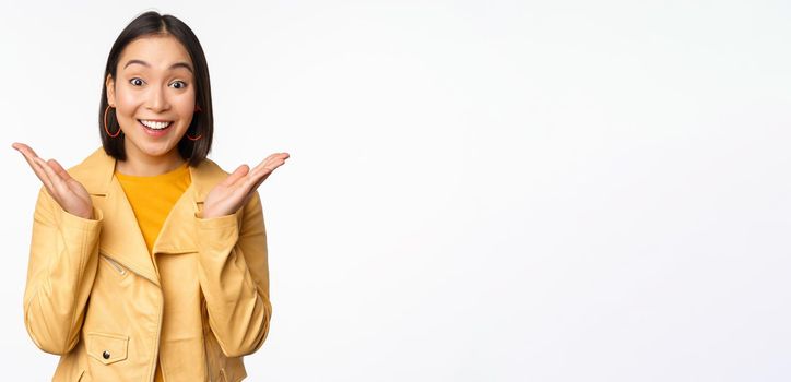 Image of asian woman looking surprised, amazed reaction, shocked face, standing over white background. Copy space