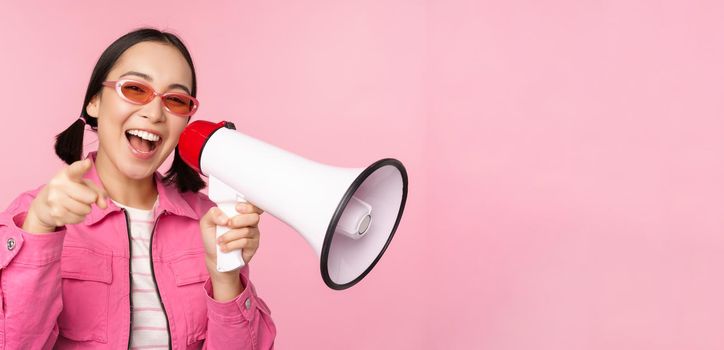 Attention, announcement concept. Enthusiastic asian girl shouting in megaphone, advertising with speaker, recruiting, standing over pink background.