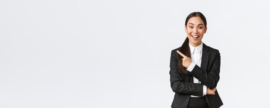 Excited attractive asian female saleswoman, real estate agent in suit suggesting perfect house, standing in suit and pointing finger left. Businesswoman making announcement, show banner.