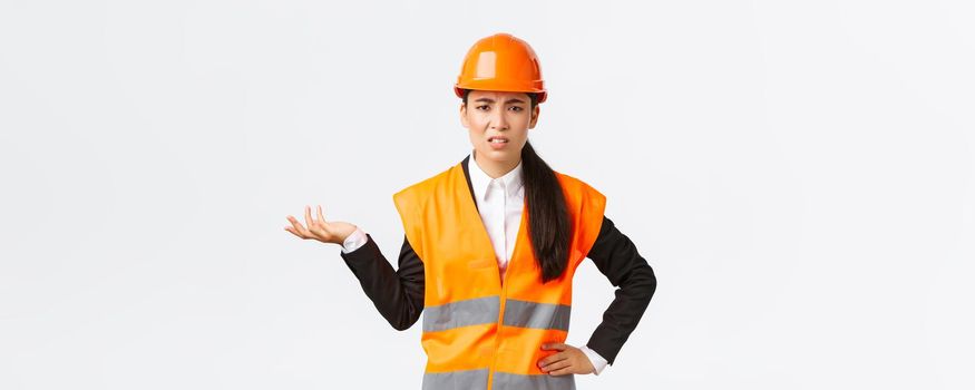 So what, wtf going on. Frustrated and disappointed asian female chief engineer complaining on employees, scolding someone, wear reflective jacket and safety helmet, raising hand confused.