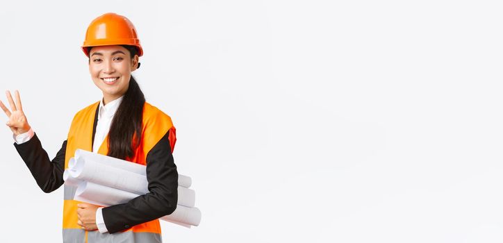 Smiling asian female architect at construction area, building estates, showing number three, carry blueprint as wearing safety helmet, giving fixed time for task done, white background.