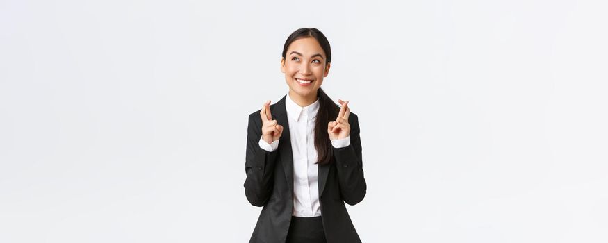 Hopeful optimistic businesswoman having faith in herself, believe dreams come true, cross fingers for good luck and looking up at sky, making wish, praying for relish, white background.