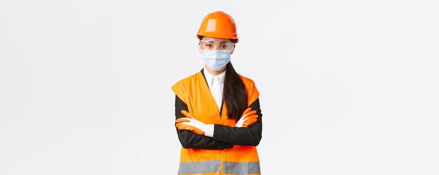 Covid-19 safety protocol at enterpise, construction and preventing virus concept. Confident asian female chief engineer looking how workers follow protocol during coronavirus, wear face mask.
