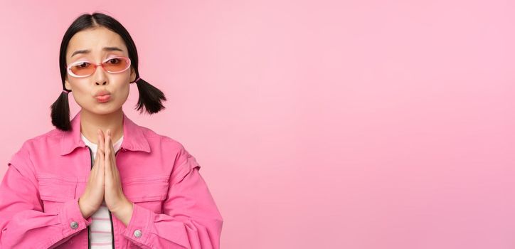 Please. Cute asian girl asking favour, begging, standing against studio background. Copy space