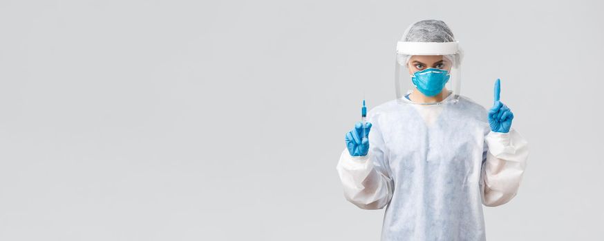 Covid-19, medical research, diagnosis, healthcare workers and quarantine concept. Determined doctor in PPE costume, personal protective equipment, hold syringe with coronavirus vaccine for patient.