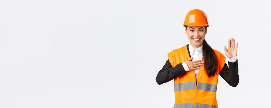 Sincere, honest and confident asian female engineer at building area, making promise, give oath to clients, looking trustworthy, standing in safety helmet, telling truth, white background.
