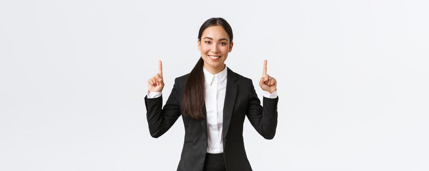 Confident good-looking asian businesswoman have great suggestion for client, pointing fingers up at announcement or special offer. Real estate agent selling house, showing banner, white background.