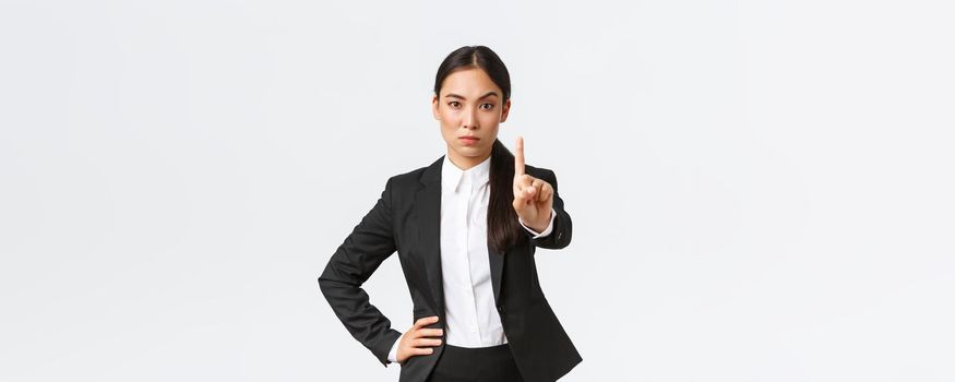 Serious angry asian businesswoman making restriction, give warning sign. Displeased saleswoman showing stop, shaking finger as scolding someone, forbid action, white background.