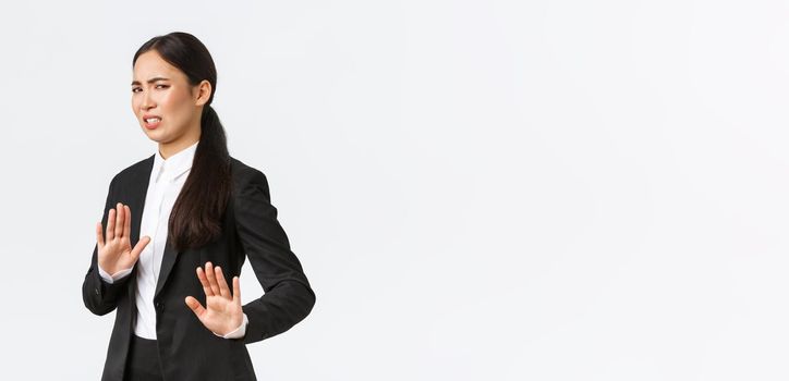 Displeased asian businesswoman avoiding risky suggestions, shaking hands in refusal, rejecting disgusting strange offer. Saleswoman grimacing from aversion and step away, white background.