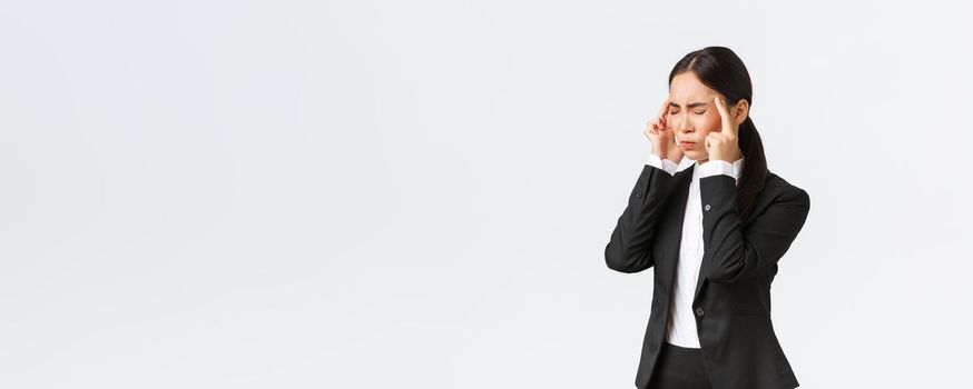 Profile of asian businesswoman in black suit having migraine, touching temples and grimacing from painful feeling in head. Female office manager having headache, need painkillers, white background.