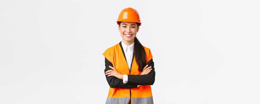 Smiling confident asian female chief manager at building, construction worker in safety helmet cross arms and looking determined. Assertive architect introduce her project to investors.