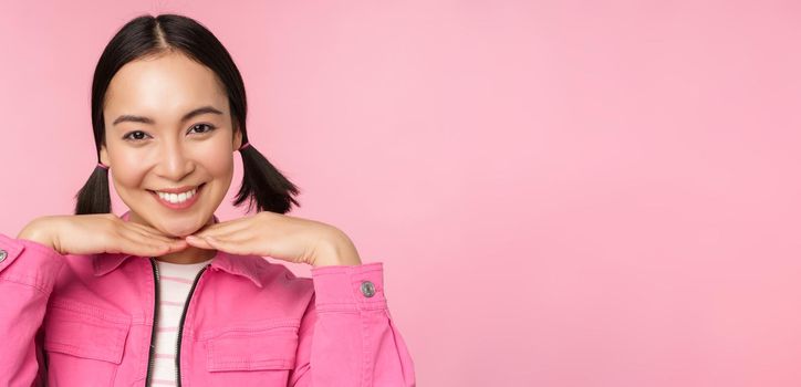 Skin care and cosmetology concept. Beautiful asian girl smiling and laughing, showing clean healthy facial skin, posing against pink background. Copy space