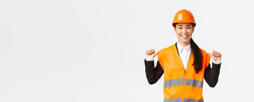 Successful proud smiling asian female construction manager, engineer in safety helmet pointing at herself, show-off. Architect recommend personal assistance, bragging accomplishments.