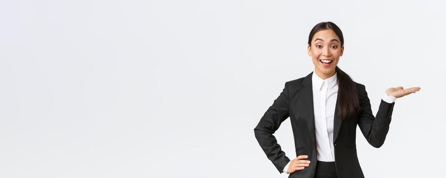 Excited smiling saleswoman introduce product, trying sell something over white copyspace. Pretty asian female manager showing project, pointing hand right and looking upbeat, white background.