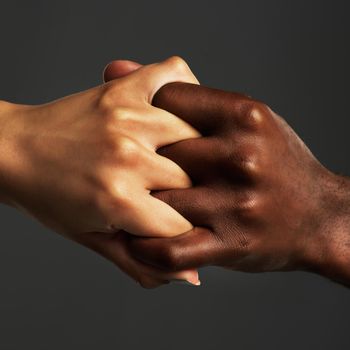 Studio shot of two unrecognizable people holding their hands together against a grey background.