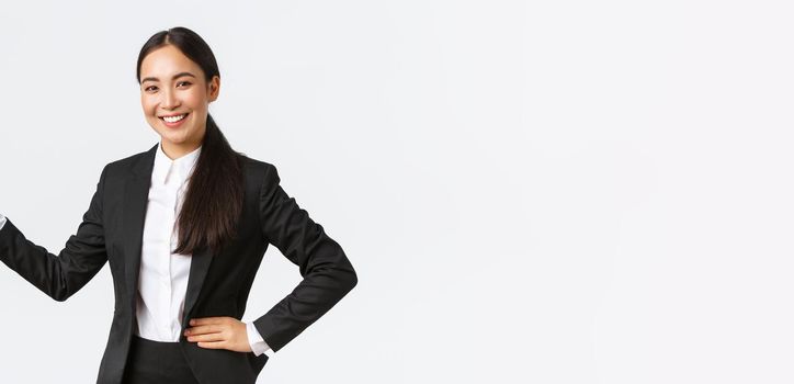 Smiling happy businesswoman in black suit pointing hand left at statistics of diagram with pleased face, having business meeting, introduce product or graph, standing white background.