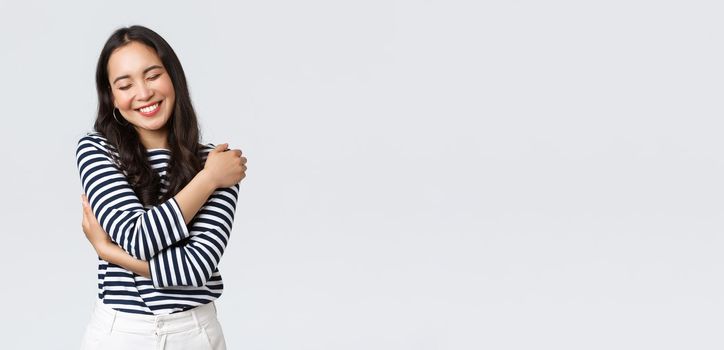 Lifestyle, people emotions and casual concept. Carefree smiling asian bodypositive girl close eyes and laughing carefree, embracing own body, love herself, white background.