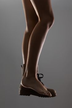 Sexy female legs wearing one waterproof boot. Side lit half silhouette.